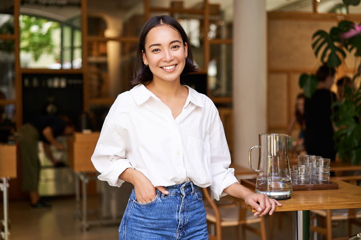 Portrait of young female entrepreneur, how to get restaurant funding, cafe owner, standing at the door entrance and smiling, looking confident